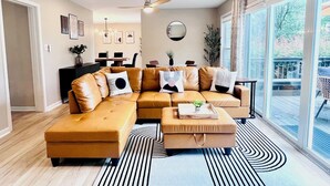 A modern living room with a sectional sofa, a coffee table, and a dining area in the background.