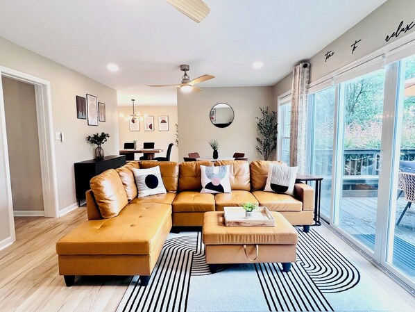 A modern living room with a sectional sofa, a coffee table, and a dining area in the background.
