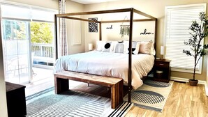 A bedroom with a four-poster bed, a ceiling fan, a bench at the foot of the bed, and a view of the outdoors.