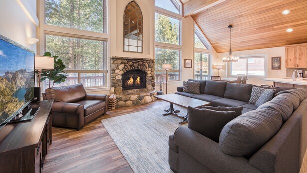 A spacious living room with a stone fireplace, large windows, and a high ceiling.