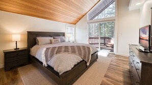 A bedroom with a wooden ceiling, a large bed, a nightstand, a dresser, and a TV.