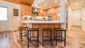 A modern kitchen with wooden cabinets, a large island with stools, stainless steel appliances, and a wooden ceiling.