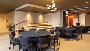A modern conference room with a large round table, multiple chairs, a staircase, and a unique chandelier.
