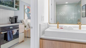 A modern bathroom with a large mirror, white sink, and gold faucets.