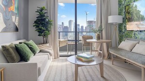 A modern living room with a sofa, a coffee table, and a view of the city skyline through large windows.