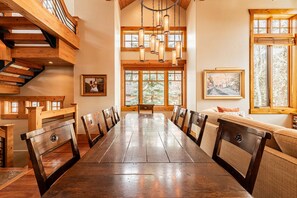 A spacious dining area with a long wooden table, multiple chairs, a staircase, and large windows with natural light. - Park City Main Street Powder Lodge / Pool Table, Ski Access, Chef (Park City)