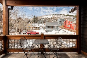 A wooden balcony with metal chairs and a table, overlooking a snowy town with buildings and a red truck. - Park City Main Street Powder Lodge / Pool Table, Ski Access, Chef (Park City)