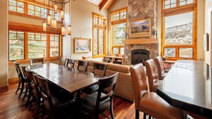 Un comedor amplio con una gran mesa de madera y sillas, una chimenea de piedra y ventanas grandes que ofrecen vistas al exterior.