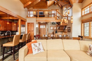 Un vaste espace de vie doté d’un haut plafond, de poutres apparentes, d’un escalier et d’une cuisine avec des meubles en bois.