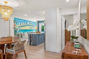 Une cuisine moderne avec un îlot central bleu, un coin repas avec des chaises en osier et une grande fresque représentant l’île d’Anna Maria.