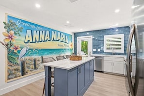 A kitchen with a large island, a mural, and a view of the outdoors. - Cozy Cabana West – AMI Pet Friendly Bungalow w/ Heated Pool & Walk to Beach (Holmes Beach)