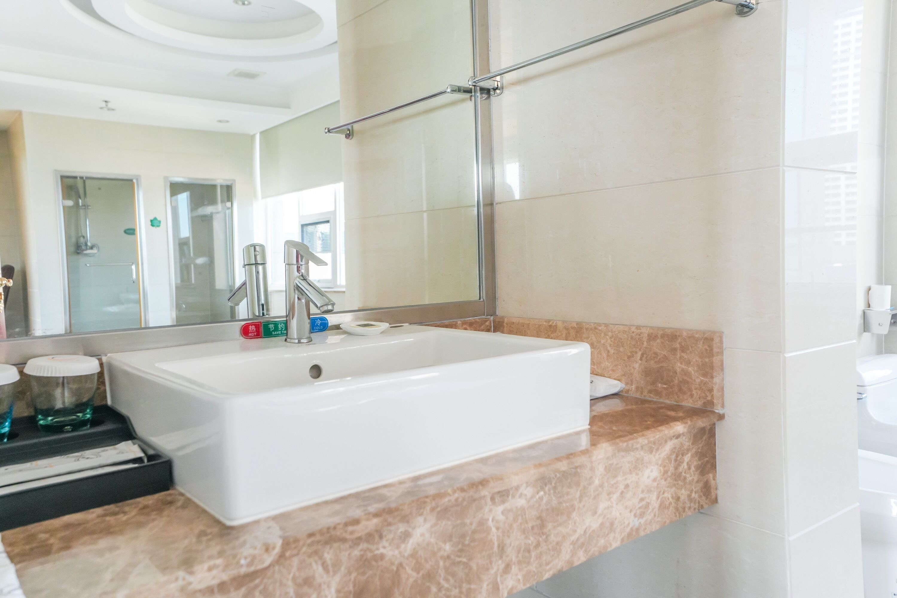 A modern bathroom with a large mirror, a white sink, and a marble countertop.