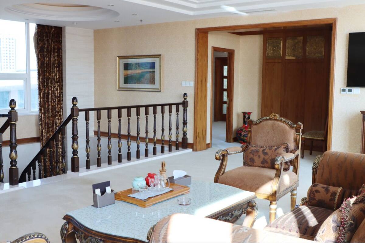 A spacious living room with a grand staircase, elegant furniture, and a large painting on the wall.