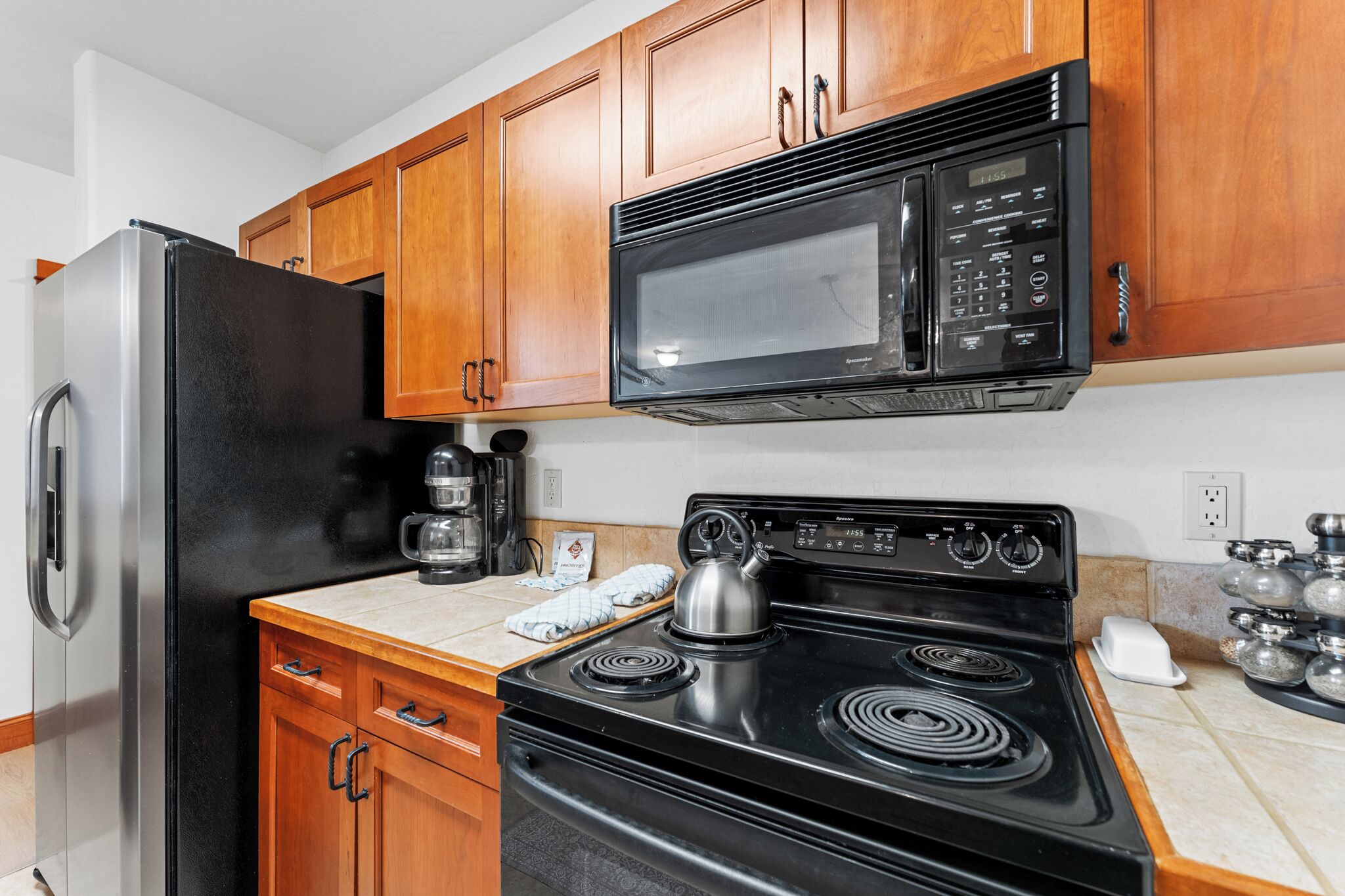 Una cocina con gabinetes de madera, un refrigerador de acero inoxidable, un microondas negro, una estufa negra y una cafetera.