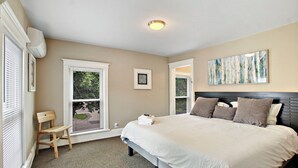 A bedroom with a large bed, a window with blinds, a chair, and a painting on the wall. - Neighboring suites in central heart of town! Perfect for couples! Walk to Town, Balcony, & Parking (Lake Geneva)