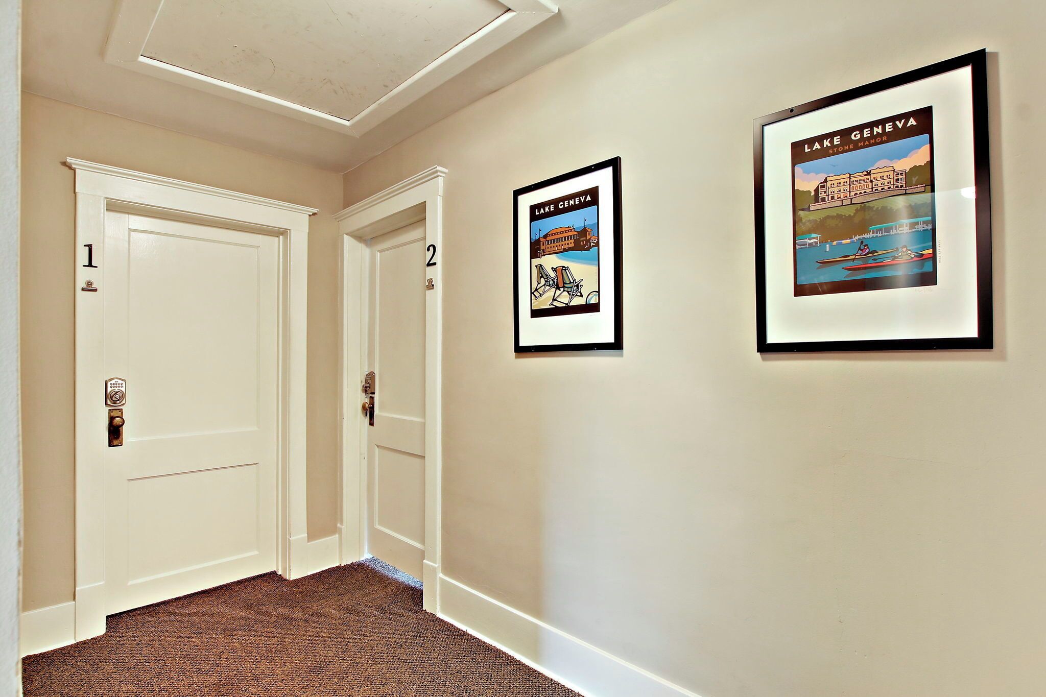 A hallway with two white doors, numbered 1 and 2, and two framed posters on the wall.