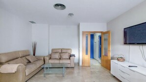 A living room with a beige sofa, a glass coffee table, a white cabinet, and a television mounted on the wall.