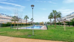 A swimming pool surrounded by grass, palm trees, and a lamp post.
