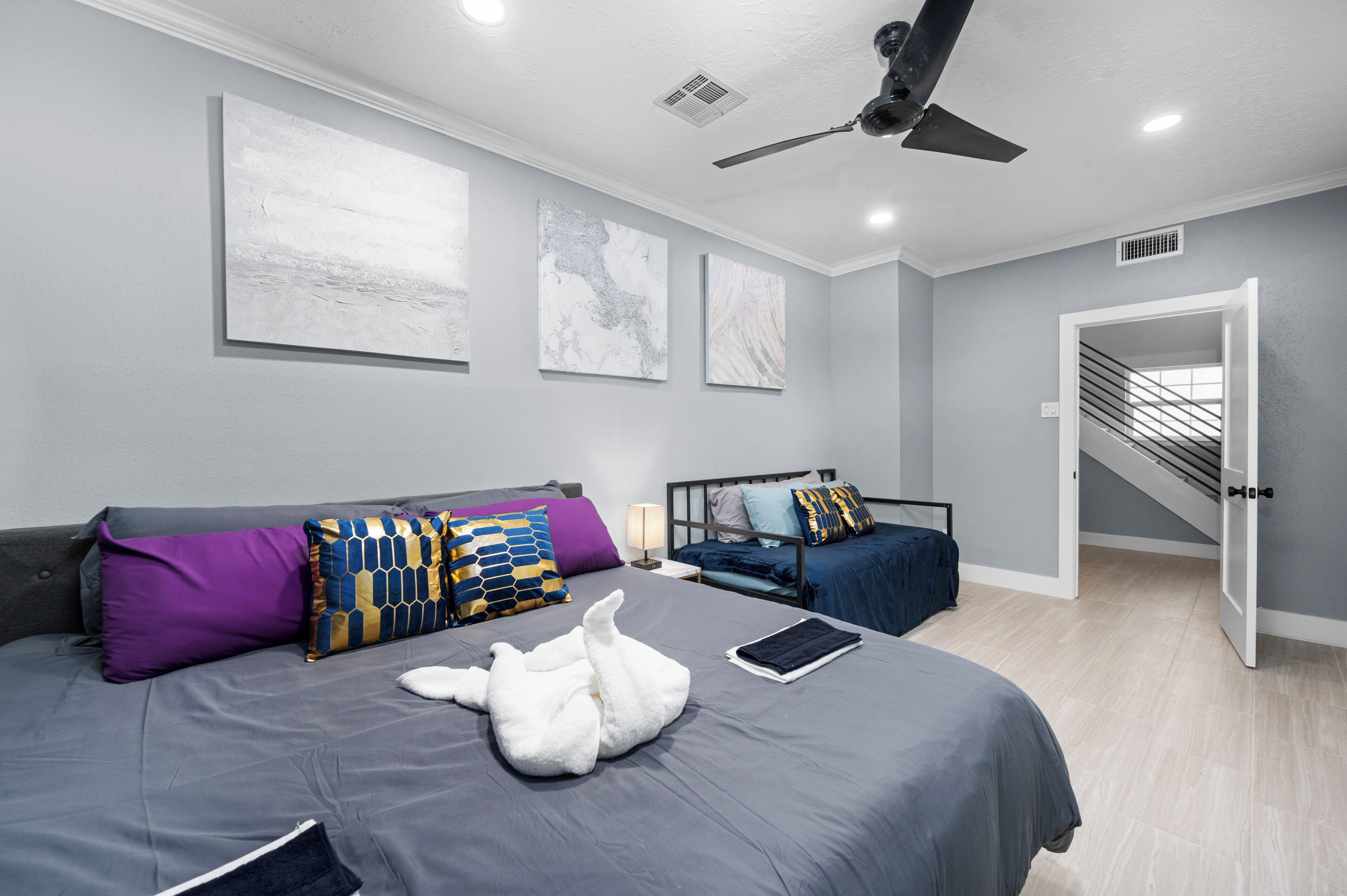 Une chambre d’hôtel moderne avec un grand lit, un ventilateur de plafond et des œuvres d’art accrochées aux murs.
