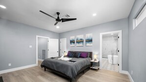Une chambre à coucher moderne, avec un lit, des tables de chevet, un ventilateur de plafond et des œuvres d’art accrochées au mur.