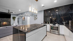 Une cuisine moderne dotée d’un îlot central, d’un four encastré et de luminaires suspendus.