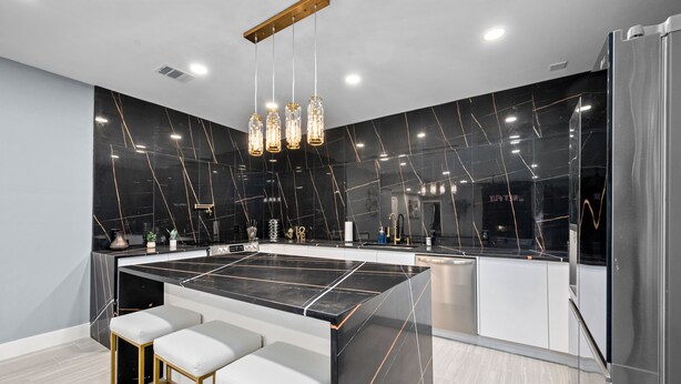 Une cuisine moderne dotée d’un îlot central, de tabourets de bar et de luminaires suspendus.