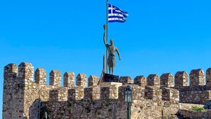 A statue of a figure holding a flag on a stone wall with crenellations.