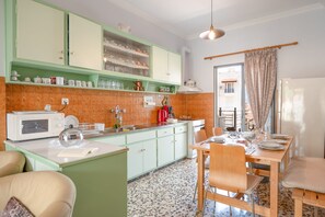 Una cocina con gabinetes verdes, un microondas blanco y un comedor con una mesa dispuesta para cuatro.