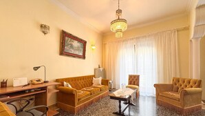 A hotel room with a sofa, armchairs, a desk, and a chandelier.