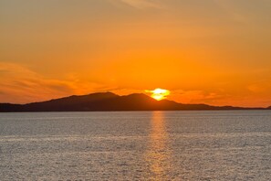 A sunset over a calm body of water with a distant mountain range.