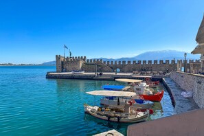 Un port où des bateaux sont amarrés, un mur de pierre et un drapeau sur une tour.
