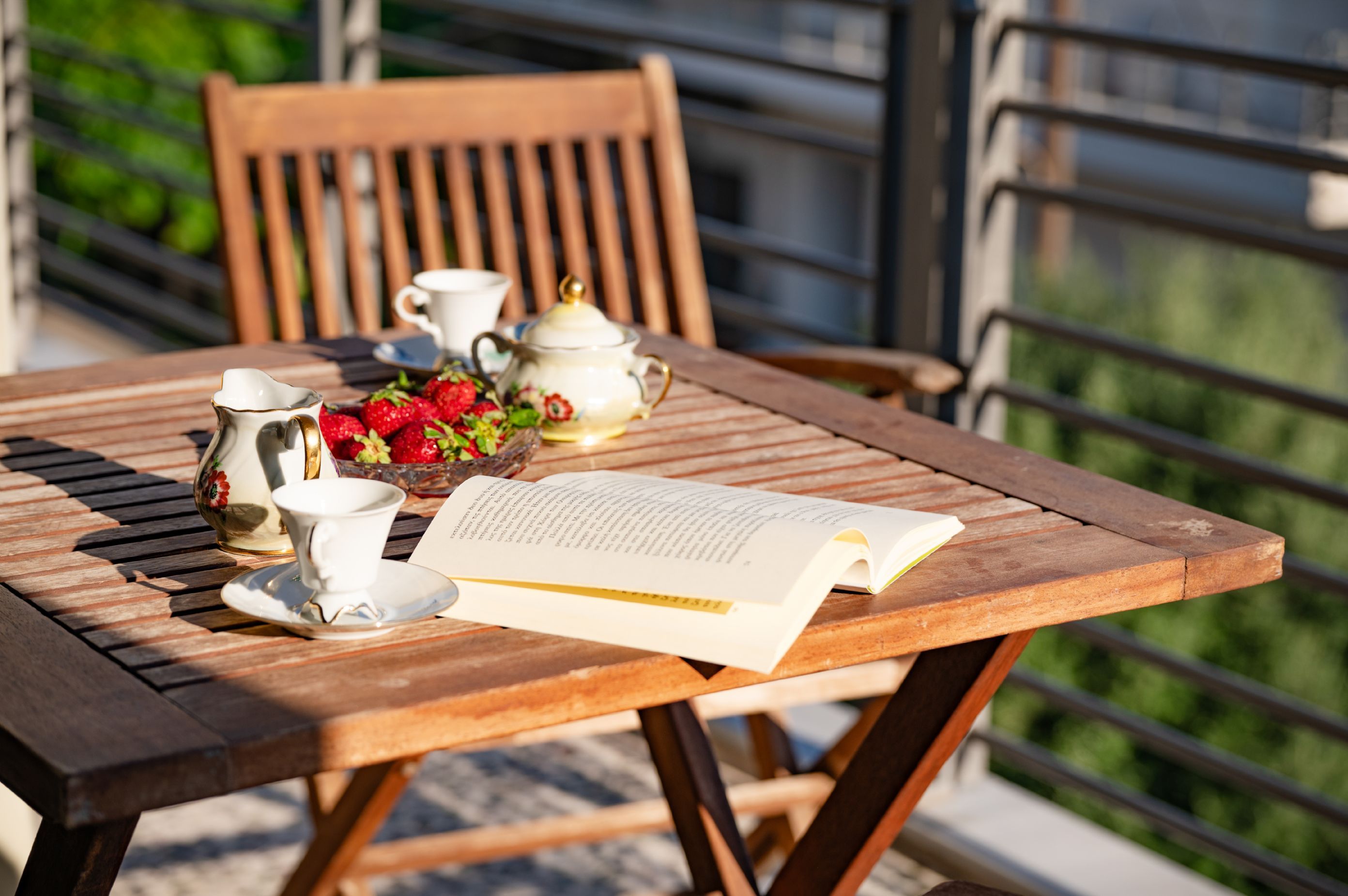 A wooden table with a book, teapot, cups, and strawberries.