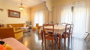 A dining area with a table set for four, surrounded by wooden chairs, a yellow sofa, and a chandelier.
