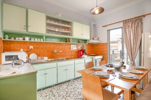 A kitchen with green cabinets, a dining table set for four, and a window with curtains. - Giorgos House: Holiday Home in Nafpaktos, Near beach, taverns, WiFi (Lagathoula)