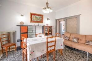 A dining area with a table set for four, a chandelier, and a painting above the table. - Giorgos House: Holiday Home in Nafpaktos, Near beach, taverns, WiFi (Lagathoula)