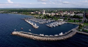 Vue aérienne d’une marina avec des bateaux amarrés, une digue et des bâtiments en arrière-plan.