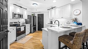 A modern kitchen with white cabinetry, stainless steel appliances, and a central island with bar stools.