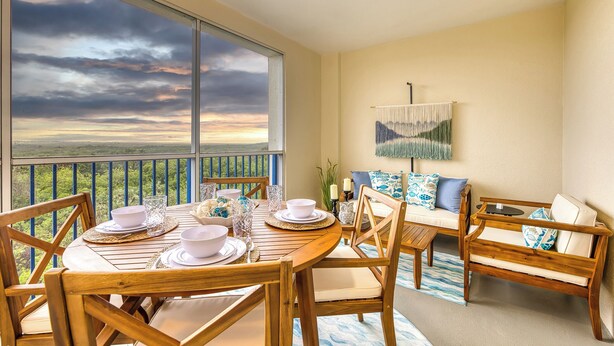 A dining area with a table set for four, a sofa, and a view of the landscape through large windows.