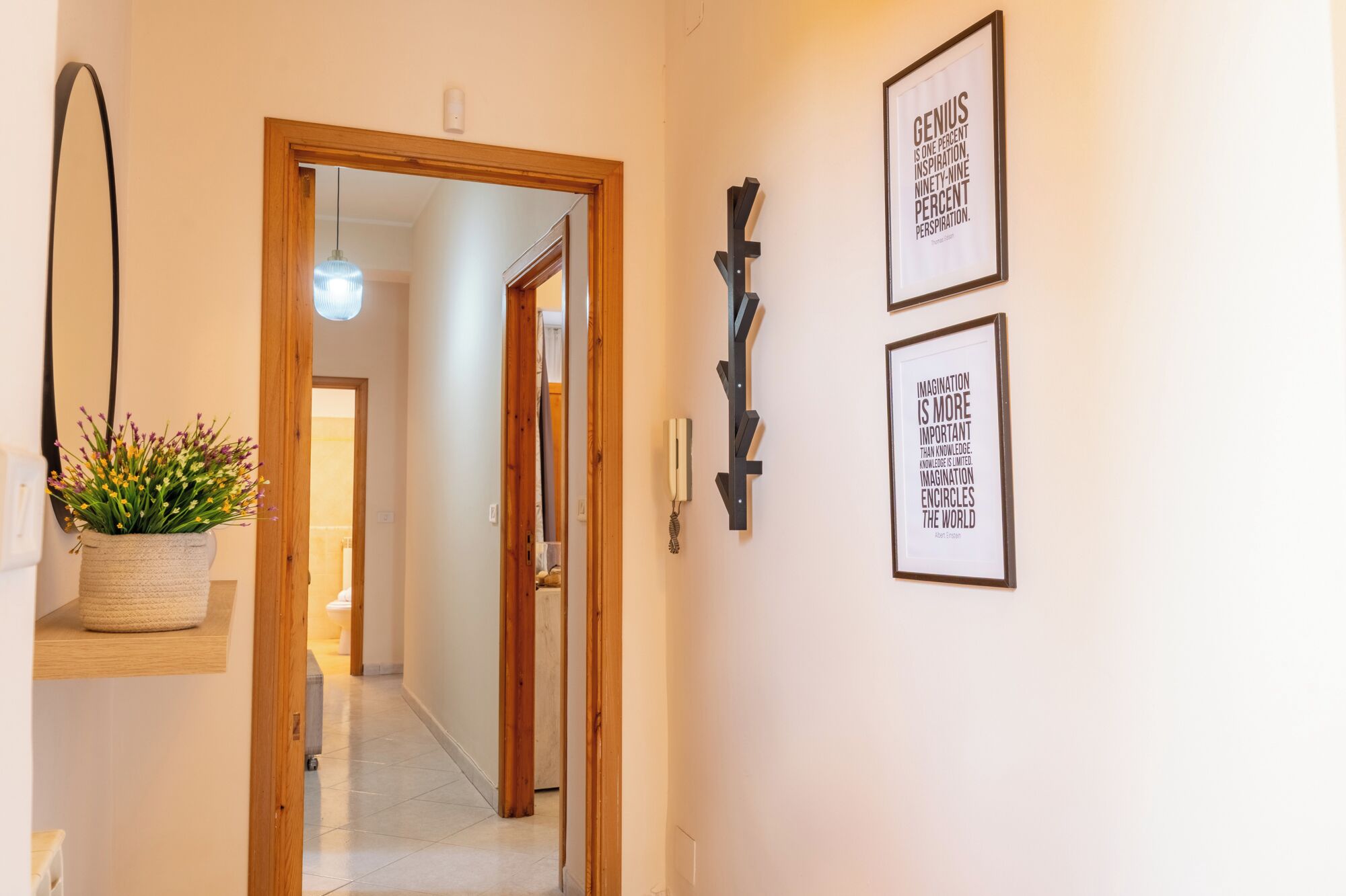 A hallway with a wooden door, a hanging plant, and two framed quotes on the wall.