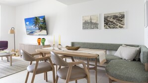 Una sala de estar moderna con una mesa de comedor, sillas, un sofá verde y obras de arte colgadas en la pared.