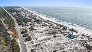 An aerial view of a coastal area with a road, beach, and several buildings. - Steps to Sand on Private Beach | Cozy 2BR Cottage (Gulf Shores)