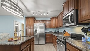 A modern kitchen with wooden cabinets, stainless steel appliances, granite countertops, and a central island with a wine bottle and glasses. - Waterfront 4BR House w/Game Rm for Fishing, Boating, & Kayaking (Gulf Shores)
