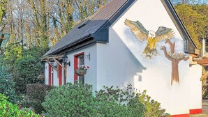 Un edificio pequeño con fachada blanca y detalles rojos, un techo inclinado y un mural de un águila.