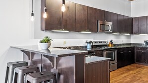 A modern kitchen with dark wooden cabinets, stainless steel appliances, and a central island with bar stools. - Stylish Industrial Loft in Downtown St. Louis (St. Louis)