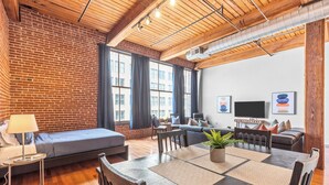 A modern living room with a brick wall, wooden ceiling, and large windows. - Stylish Industrial Loft in Downtown St. Louis (St. Louis)