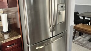 A stainless steel refrigerator with a control panel, a wooden countertop, and a dining area with a table and chairs. - Charming 3-bedroom house with Pool, Washer and Dryer and Garage in Boca Raton (Boca Raton)
