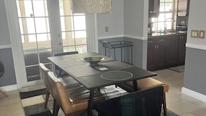 A dining area with a rectangular table, six chairs, a patterned hanging light fixture, and a kitchen in the background. - Charming 3-bedroom house with Pool, Washer and Dryer and Garage in Boca Raton (Boca Raton)