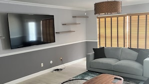 A modern living room with a flat-screen TV mounted on the wall, a grey sofa, a coffee table, and a patterned rug. - Charming 3-bedroom house with Pool, Washer and Dryer and Garage in Boca Raton (Boca Raton)
