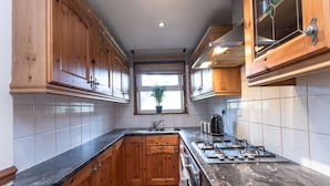 A kitchen with wooden cabinets, a gas stove, a sink, and a window with a plant.