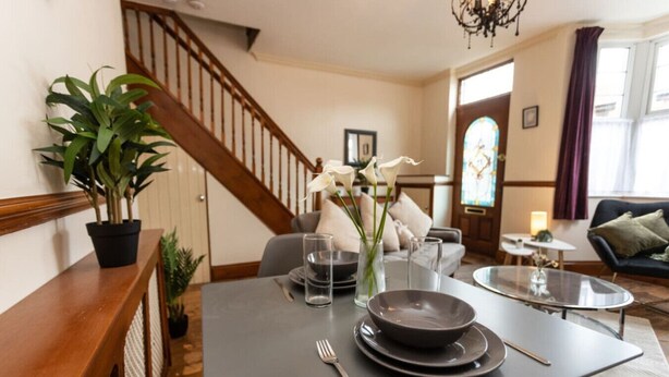 A dining area with a table set for two, a staircase, a sofa, and a stained glass window.